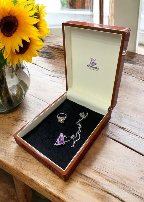 Open wooden eMemorybox on a table with a ring and a butterfly necklace inside, sunflowers in a vase behind