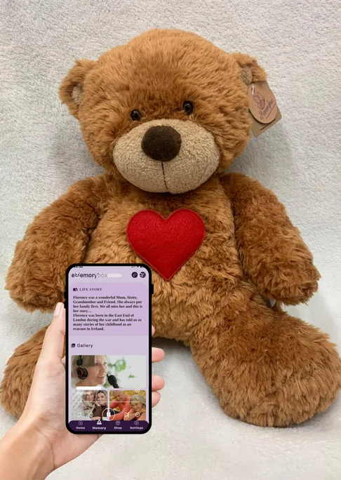 eMemorybear with a phone held in front of it showing a memorial page in the eMemorybox app