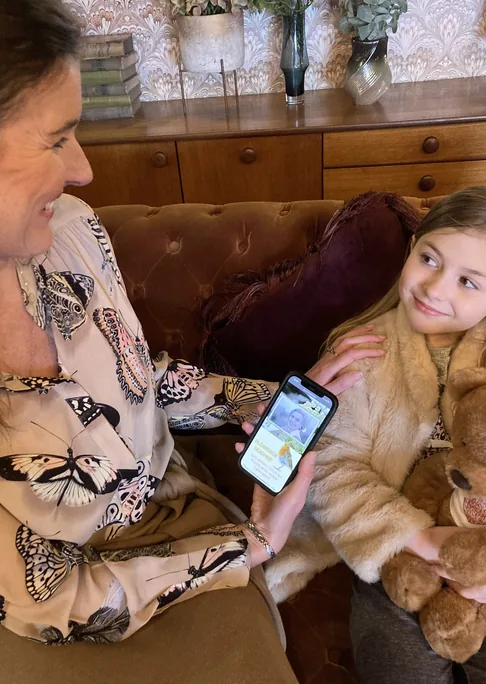 A woman and a child on a sofa looking at memories on a phone, with a teddy bear beside them