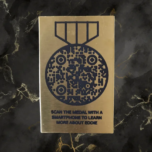 Brass memorial plaque with a medal-shaped QR code: scan the medal with a smartphone to learn more about Eddie